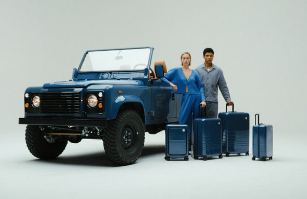 A woman and man stand beside the custom Arles Blue Land Rover Defender 90 with the full Arles Blue Glossy luggage collection.