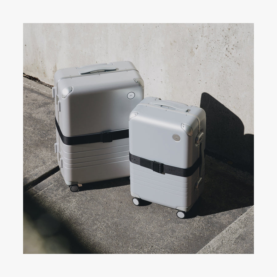 Midnight Black | Front view of two different sizes of Aluminum suitcases on the street with the Midnight Black Luggage Strap secured around them
