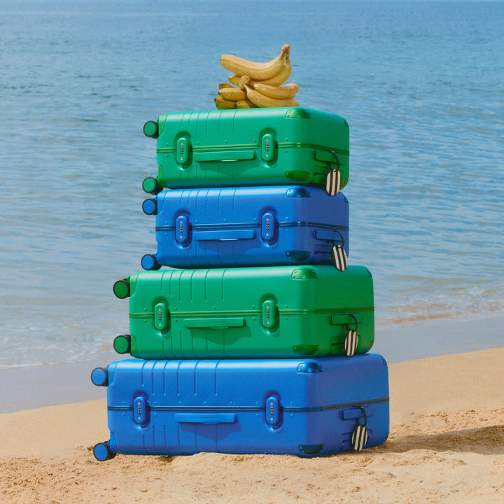 Stack of blue and green suitcases with bananas on a beach