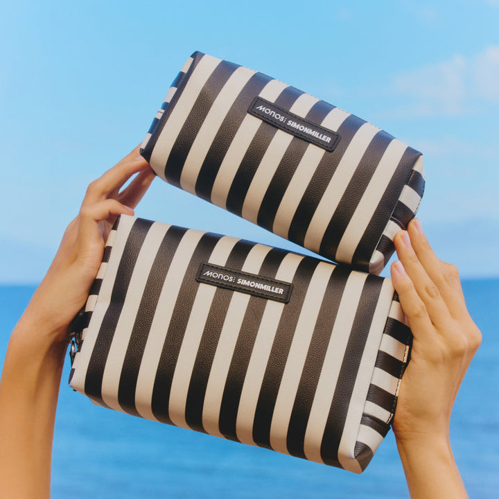 Two black and white striped pouches held by hands with a blue sky background