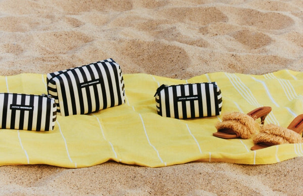 Yellow blanket with black and white striped bags and brown sandals on the beach