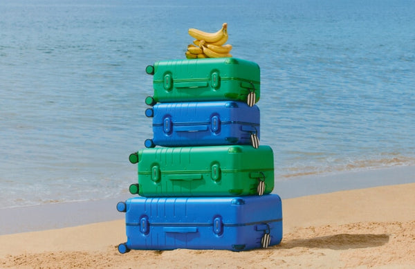 Stack of blue and green suitcases with bananas on a beach