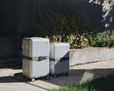 Hybrid suitcases in Silver with Luggage Strap in Olive Green under natural light.