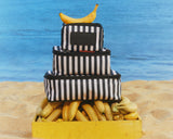 Stack of black and white striped packing cubes with bananas on a beach