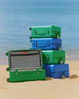Stack of green and blue suitcases on a sandy beach with ocean in the background